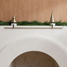 three brass cones on top of a white wall with greenery in the middle and below