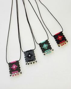 four beaded necklaces hanging from black cords on a white surface, one with pink and blue beads