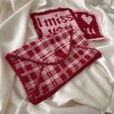 two crocheted red and white items laying on top of a bed covered in sheets