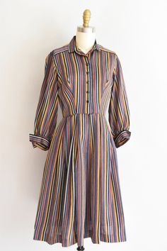 "Vintage 1950s cotton daydress. Vertical stripes in gold, black, grey, blue, green and red. Pointed v collar, longer sleeves, darted bust and nipped waist. Full skirt. Front zipper and (new) button closure. State of garment | excellent Measurements ✂--- best fit | extra small bust | up to 36 \" shoulders | 15\" shoulder to waist | 15 \" sleeves | 18\" waist | 25\" hips | free total length (shoulder to hem) | 39.5\" tag | Neiman Marcus ★★Visit The Shop★★ http://www.etsy.com/shop/seaofvintage ➸ Fi Long Sleeve Cotton Dress With Striped Collar, Cotton Long Sleeve Dress With Striped Collar, Cotton Dress With Striped Collar And Long Sleeves, Classic Striped Cotton Dress, Vintage Striped Fitted Dress, Vintage Long Sleeve Striped Dresses, Retro Fitted Dress With Vertical Stripes, Fitted Retro Dresses With Vertical Stripes, Vintage Striped Dress For Work