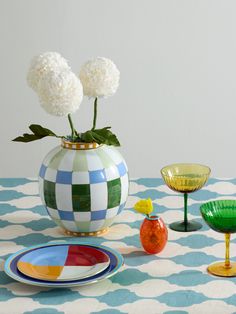 a table topped with plates and vases filled with flowers on top of a blue and white checkered table cloth