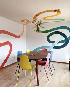 a dining room table with colorful chairs and a chandelier hanging from the ceiling