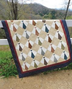 a quilt hanging on a fence with trees in the background