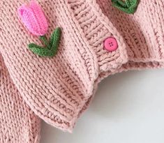 two knitted sweaters with pink flowers on them and green leaves attached to the sleeves