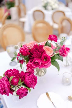 pink flowers are in vases on a white table cloth with silverware and napkins