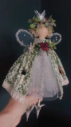 a hand holding an angel doll with flowers on it's head and wings, in front of a black background