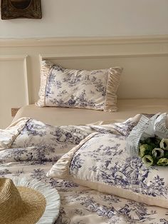 a bed with blue and white comforters, pillows and a straw hat on it