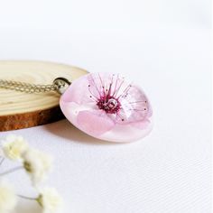 a pink flower on a chain next to some white flowers and a piece of wood