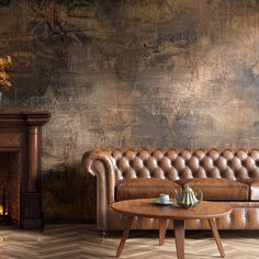 a brown leather couch sitting in front of a fire place next to a wooden table