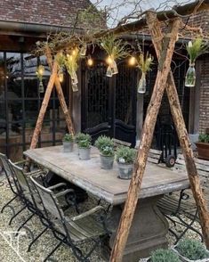 an outdoor dining area with potted plants on the table and lights hanging from the roof