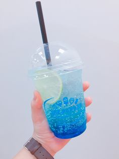 a hand holding a blue and green drink with a lime slice in it's cup