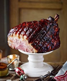 a large piece of meat sitting on top of a white cake plate next to other food