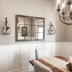 a dining room table and chairs with a mirror on the wall above it, along with hanging candle holders