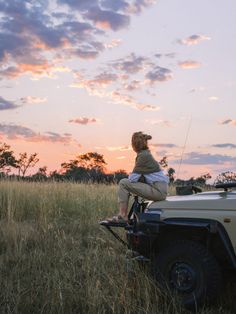 a man sitting on top of a vehicle in the middle of a field at sunset