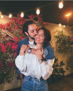 a man and woman standing next to each other in front of some flowers at night