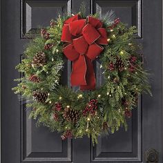 a christmas wreath with red bow and pine cones hanging on the front door to give it a festive feel