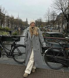 a woman standing next to a bike on a brick walkway in front of a canal