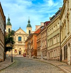 an empty cobblestone street in the middle of some old buildings with steeple tops