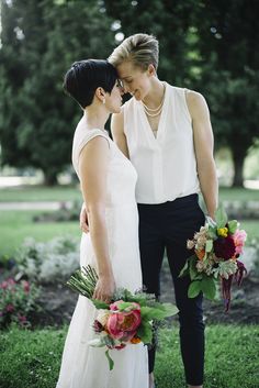 two women standing next to each other in front of trees and grass holding bouquets