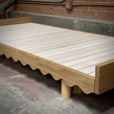 a large wooden bed frame sitting in front of a brick wall with pipes coming out of it