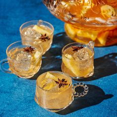 three glasses filled with drinks sitting on top of a blue tablecloth next to a pitcher