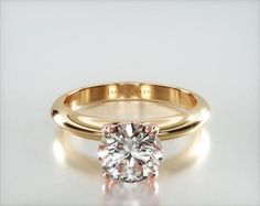 a yellow gold engagement ring with a round cut diamond in the center, on a white background