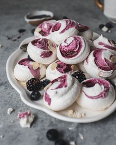 a white plate topped with lots of pastries covered in pink icing and blackberries