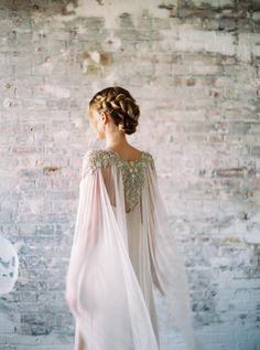 a woman standing in front of a brick wall wearing a white dress with long sleeves