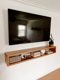 a flat screen tv mounted to the side of a wall next to a wooden shelf