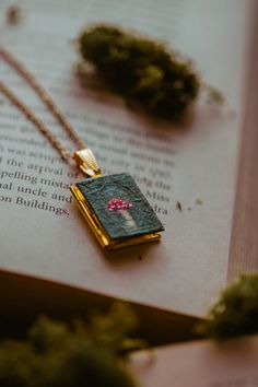 two necklaces sitting on top of an open book with moss growing out of it