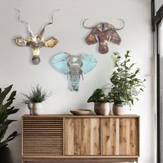 an elephant head is mounted on the wall above a wooden cabinet with potted plants