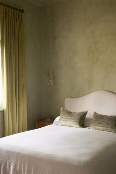 a white bed sitting in a bedroom next to a window with yellow drapes on it