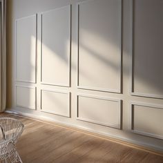 an empty room with wooden floors and white paneling on the walls, along with a wicker chair