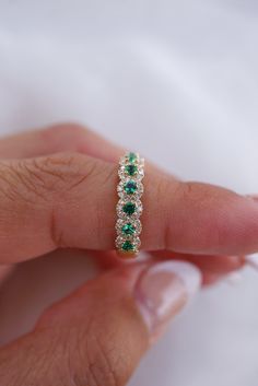 a woman's hand holding a ring with emeralds and white diamonds on it