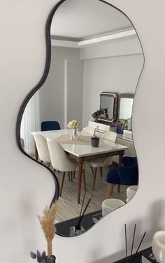 a mirror reflecting a dining room table with blue chairs and a vase on the side