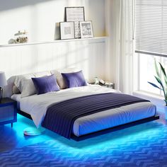 a bed with blue lights on the floor in a white room next to a window