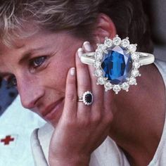 an older woman wearing a blue ring with diamonds on it and holding her hand up to her face