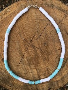 a white and blue beaded necklace sitting on top of a piece of tree trunk