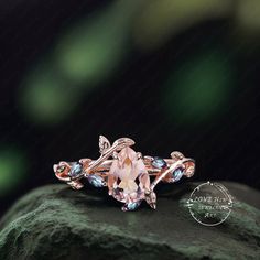 an engagement ring with pink and blue stones on top of a green mossy rock