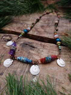 a necklace with shells and beads is on a piece of wood in front of some grass