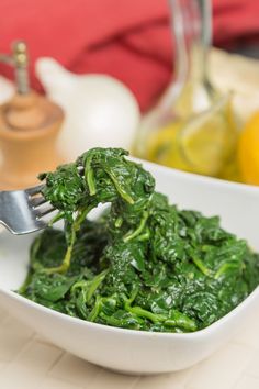 a white bowl filled with spinach on top of a table next to lemons