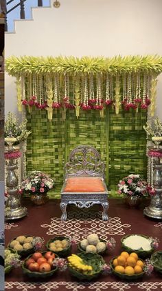 an arrangement of fruits and vegetables on a table in front of a green wall with flowers