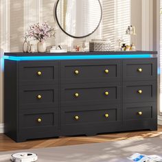 a black dresser with gold knobs and blue light under the top, in front of a window