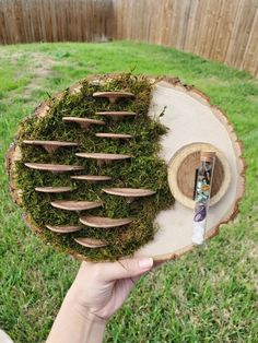 a person holding a piece of wood with moss growing on it in the middle of a yard