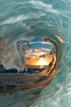 an ocean wave with the sun setting in the background and some water swirling around it