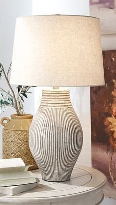 a table with a lamp, vase and books on it in front of a painting