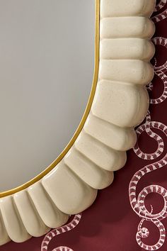 an oval mirror with gold trim on a red wallpapered surface, next to a snake - patterned table cloth