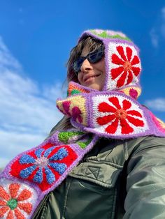 a woman wearing a crocheted scarf with flowers on it and a hood over her head