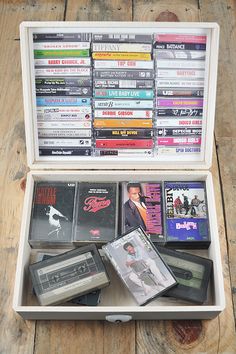 an open white box filled with various cd's on top of a wooden floor