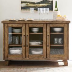 a wooden cabinet with glass doors and plates on the bottom, next to a painting